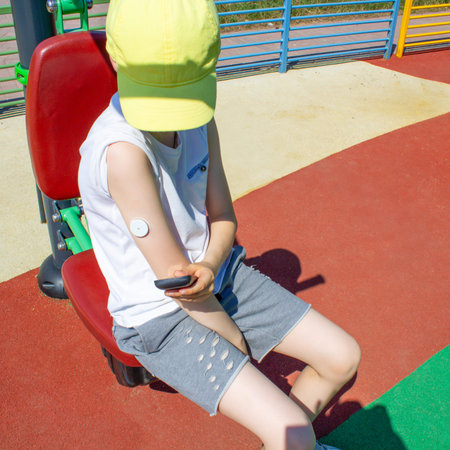 Child With Glucose Sensor On Arm Checking Blood Sugar Level At Outdoor Playground. Concept Of...