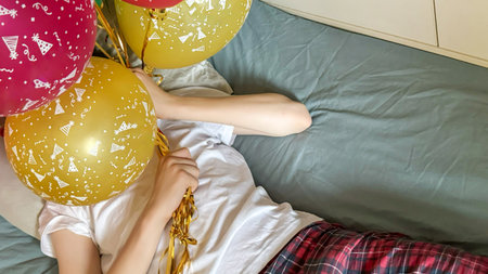 Teen Hiding Face Behind Balloons In Bed During Daylight For Concepts Of Social Fatigue, Birthday Anxiety, Introversion, Celebration Burnout, And Emotional Overload In Youth Lifestyle Visual Narrativesの写真素材