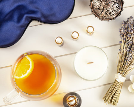 Self-care flat lay with blue sleeping mask, lavender flower, herbal tea with lemon and natural oils on a white wooden tray. Concept of Me time. Remedy for healthy sleepの写真素材