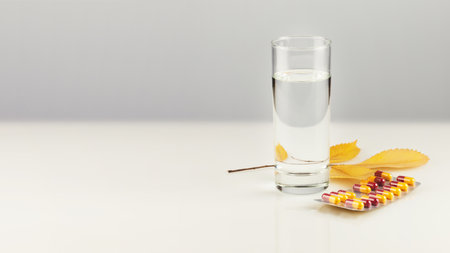 Health care autumn banner with pills, full glass of pure water and autumn leaves on white table with copy space. Concept of flu season and no virus. Vitamins and nutrients in capsules for good healthの写真素材