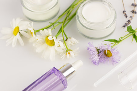 Jars with organic creams, bottle with serum and wild flowers on a white background. Concept of wild-harvested beauty and natural cosmetics based on a wild plant. Soft focus styleの写真素材