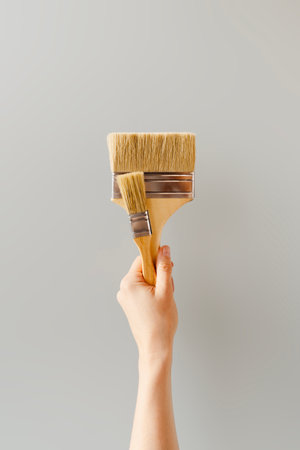 Hand Holding Paintbrushes Against Neutral Wall Backgroundの写真素材