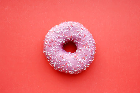 Pink donut with sprinkles on red background. top view.の写真素材