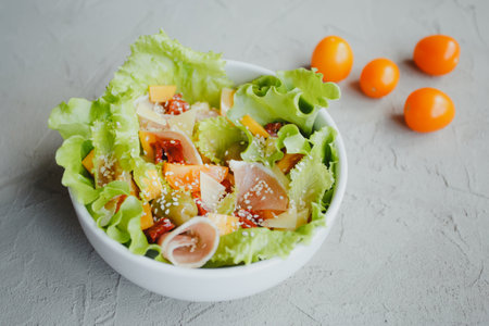 Fresh salad of lettuce, cherry tomatoes, olives, sun-dried tomatoes, Parma ham, cheddar cheese, parmesan, olive oil and sesame. Healthy eating conceptの写真素材