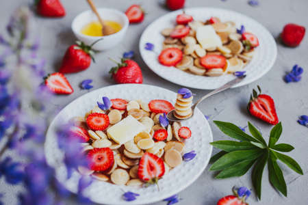 Pancake cereal, trendy food. Mini cereal pancakes with butter, honey, and strawberries.の写真素材