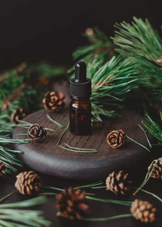 Pine essential oil in a glass brown bottle with a pipette, against the background of pine branches and cones.の写真素材