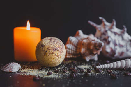 Bath bomb and coffee beans, with seashells and burning candles, on a dark background. Spa concept.の写真素材