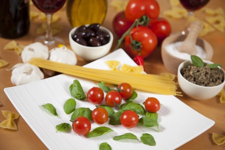 Basil and cherry tomatoes on a plate surrounded by some ingredientsの写真素材