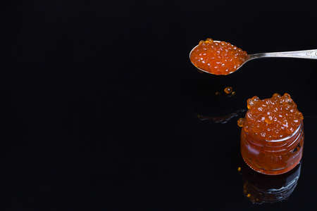 Red caviar in a jar and a spoon. Red caviar on a black background. Salmon caviar close-up. Deli. gourmet food. caviar texture. seafood. copy space, defocusの写真素材