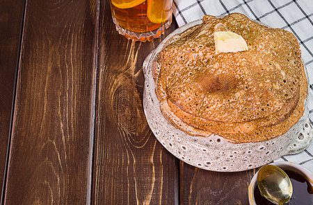 Russian pancakes with butter on a white dish and a dark wooden background close-up, isolate