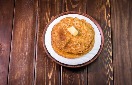 Russian pancakes with butter on a white dish and a dark wooden background close-up, isolate top view