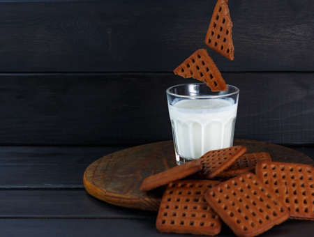 Broken chocolate cookies. cookie levitation. chocolate Cookies fall into glass with milk or kefir or cream on dark wooden background. selective focus, rustic style, low keyの写真素材