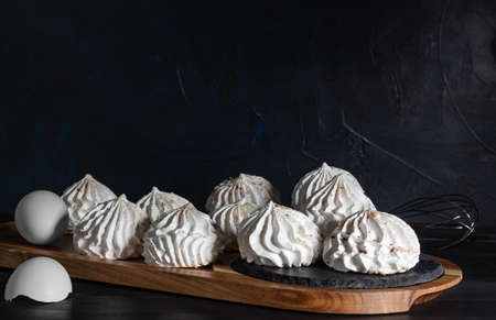 meringue and eggshell on wooden board on dark background, low kay, selective focus. Sweet meringue, delicious and light dessert. Still life in style of food.の写真素材
