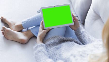 Woman at home relaxing reading on the tablet computer with pre-keyed green screenの写真素材