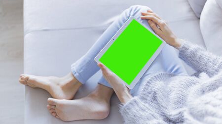 Woman at home relaxing reading on the tablet computer with pre-keyed green screenの写真素材