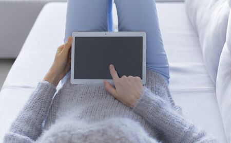 Woman at home relaxing reading on the tablet computerの写真素材