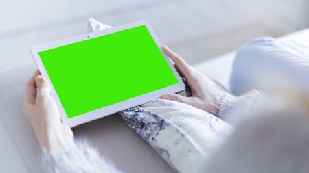 Woman at home relaxing reading on the tablet computer with pre-keyed green screenの写真素材