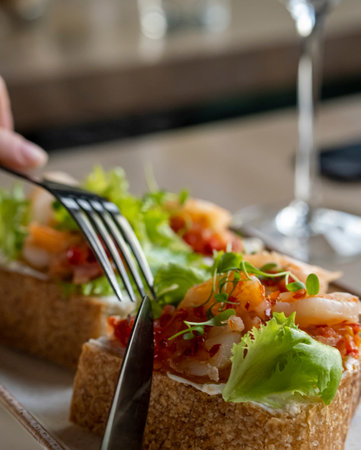Bruschetta with shrimps in a sweet and sour sauce, fresh herbs. The girl eats bruschetta in a cafe, in a restaurant. Delicious shrimp on a sandwich. One girlの写真素材