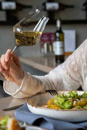 A girl has lunch in a restaurant with a glass of dry white wine. Lunch of fresh salad and wine. Restaurant life, vibes One girlの写真素材