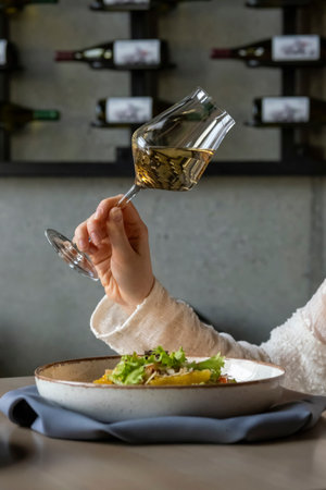 A girl has lunch in a restaurant with a glass of dry white wine. Lunch of fresh salad and wine. Restaurant life, vibes One girlの写真素材