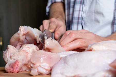 A male cook cuts fresh homemade chicken on a wooden board. Butchering the chicken in part breast, wings, legs.の写真素材