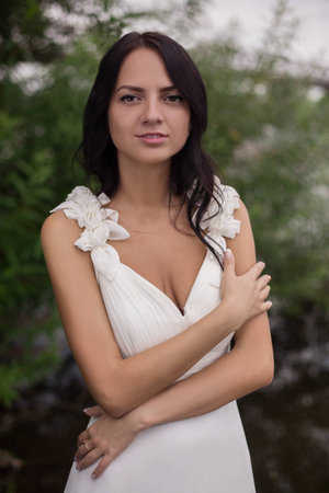 dark-skinned, dark-haired girl in a white dress near the pond. beautiful young bride on the river bankの写真素材