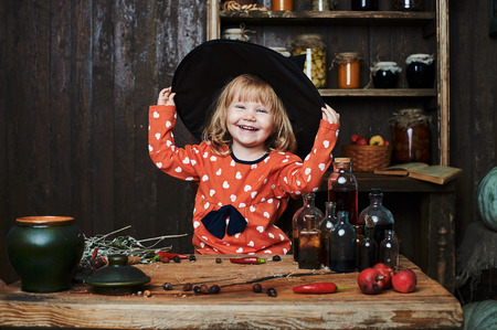 Little girl witch in black pointed hat over wooden table and magical accessories. Halloween, the studio evening.の写真素材