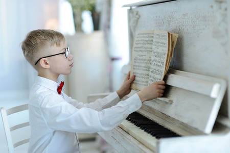 elegant boy in white shirt and glasses plays the pianoの写真素材