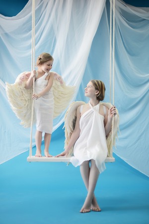 two angels swinging on a swing in heavenの写真素材