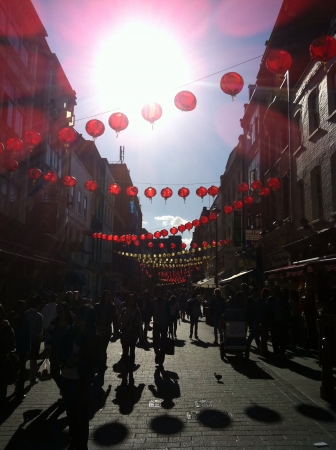 Walking down streets of Chinatown in London. Hanging lanterns are above with bright afternoon sun. の素材