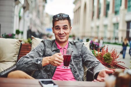 a happy young man is sitting in a cafe with a drinkの写真素材