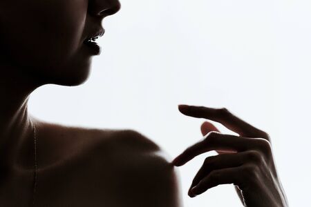 The girl touches her shoulder with her fingers. Dark portrait on a white backgroundの写真素材