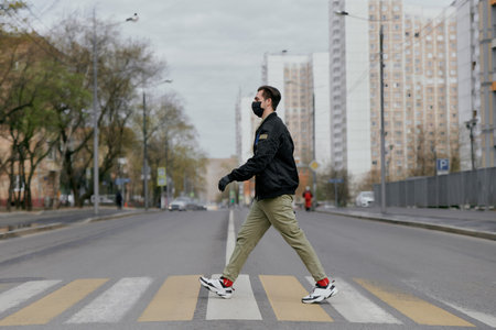 A man in a protective mask crosses the road at a pedestrian crossing