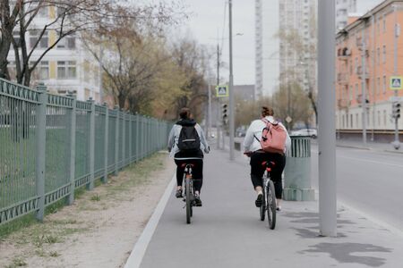 Two women ride bicycles on the sidewalkの写真素材