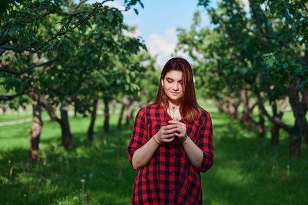 a young girl in a black and red checked shirt with red hair stands on a natural green background in...