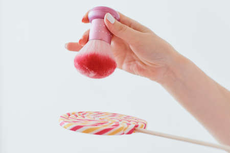 A pink manicure, powder or talc brush pours white talc on a round bright caramel candy on a stickの写真素材