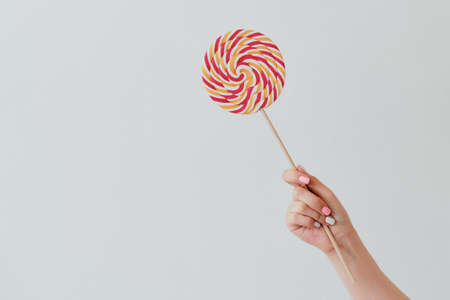 round caramel sweet candy on a stick is in the hand of a girl with a manicure on a clean light gray backgroundの写真素材