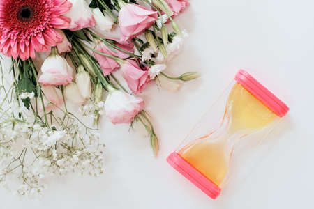 transparent hourglass pink color lies on a gray background along with a bouquet of roses and gerbera. Background for a cosmetologist or manicure masterの写真素材
