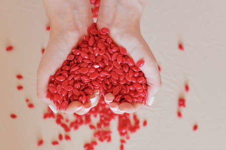 a handful of red warm wax in heart shaped pellets in the hands of a close upの写真素材