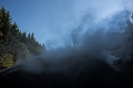 Silhouette of wood charcoal maker at work on a pile of wood burning slow. This is the traditional way of Producing charcoal.の写真素材
