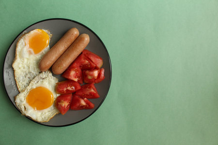Breakfast food on a gray plate on a green background sausages tomatoes scrambled eggs fried eggs...