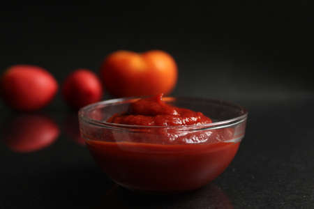 a glass saucepan with red tomato vegetable sauce stands on a black background in the background next to vegetables tomatoes red orange and onions in a yellow husk with copy spaceの写真素材