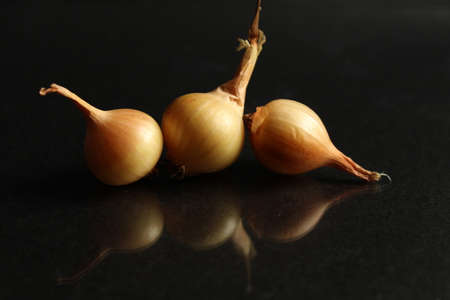 three vegetables onion bulbs in yellow orange husk on black background food background with reflexの写真素材