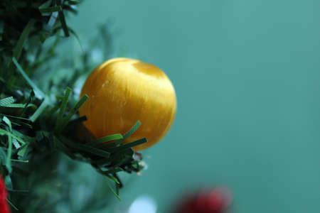 yellow new year's Christmas ball on a branch of spruce pine close up on a green turquoise backgroundの写真素材