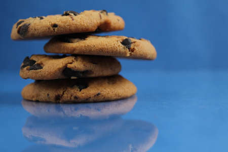 a round cookie with chocolate drops is stacked on top of each other on a blue bright saturated background with a reflection side view of copy spaceの写真素材