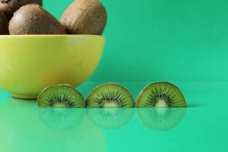 still life kiwi fruit in a yellow bowl plate and next to a kiwi copyspace slice.の写真素材