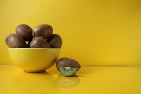 Still life of fruit trending illuminatiited yellow kiwi in a bowl plate of yellow and next pieces of kiwi yellow background copyspace.の写真素材
