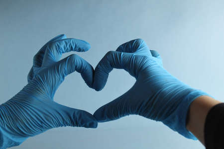 Hands doctor or nurse in blue medical gloves show of heart love on a light blue background with a place to text a copyspace.の写真素材
