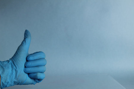 A woman 's hand in a silicone medical glove with her thumb raised up. A finger figure marking Everything is great. The white isolated background. The coronavirus protection trend is COVID-19.の写真素材