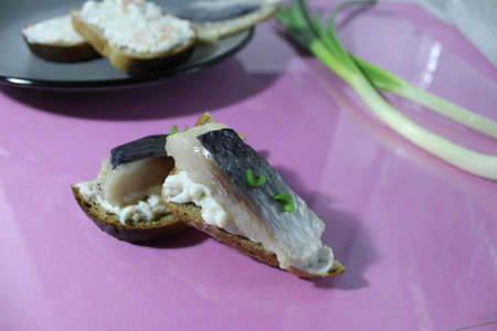 a canape sandwich with salted herring and bread next to a green onion on a lilac purple background.の写真素材